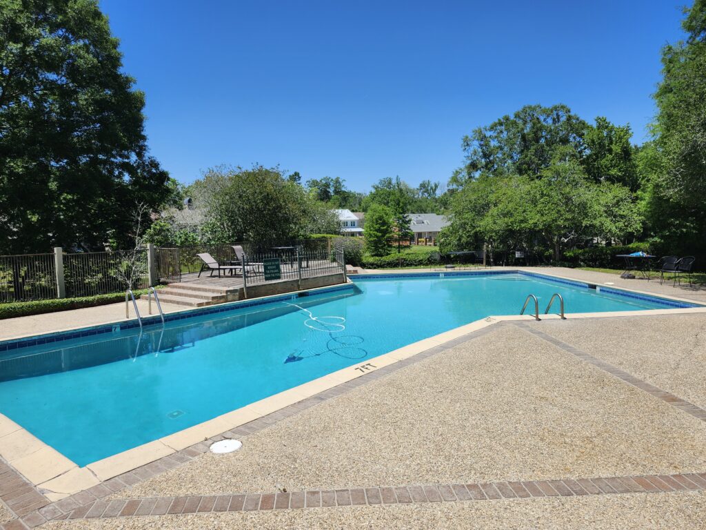 Outdoor swimming pool with clear blue water surrounded by a paved area and lounge chairs. Trees and a house are visible in the background, showcasing the elegance of Baton Rouge real estate.