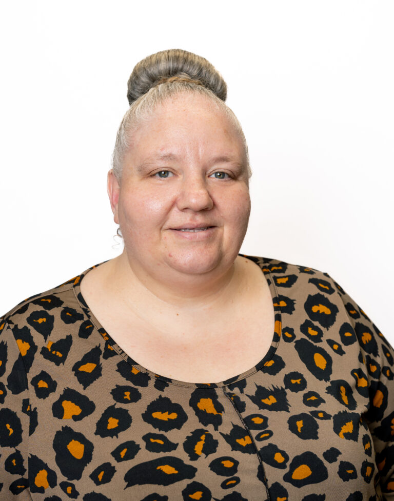 A person with a bun hairstyle wearing a leopard print blouse stands against a white background, smiling with a neutral expression. They're an employee of a prominent Baton Rouge real estate agency, specializing in property for lease.